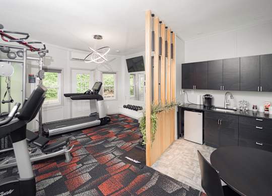 a gym with a reformer exercise machine and a kitchen with black cabinets at Woodbury Knoll, Woodbury, CT 06798