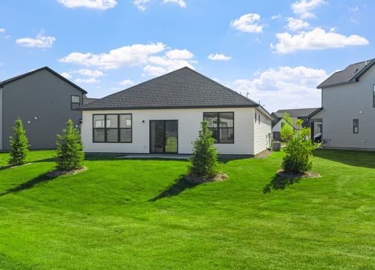the front of a house with a green lawn and some small trees