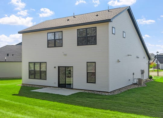 the back of a white house with a lawn and a driveway