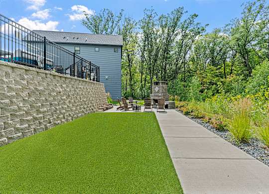 A backyard with a stone wall and a concrete walkway.