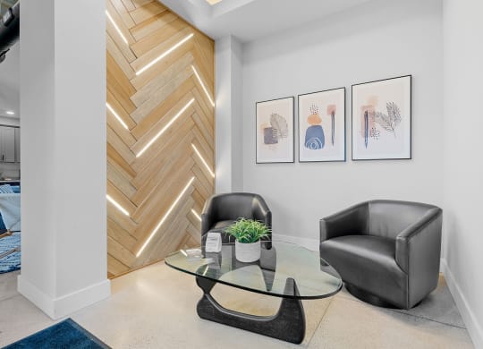 a living area with a glass coffee table, two black chairs, a chevron wood