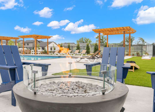 a fire pit with blue chairs around it near a pool