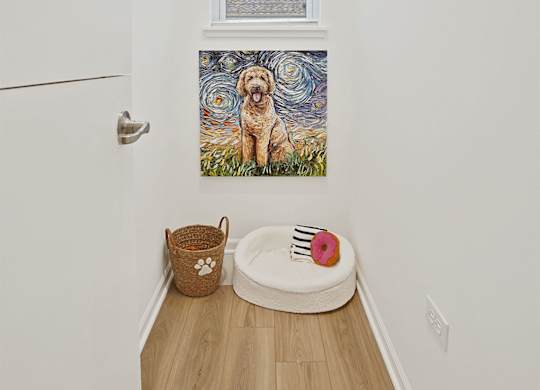 A dog painting hangs on the wall above a dog bed.