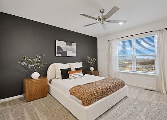 A bedroom with a large bed, a ceiling fan, and a window with blinds.