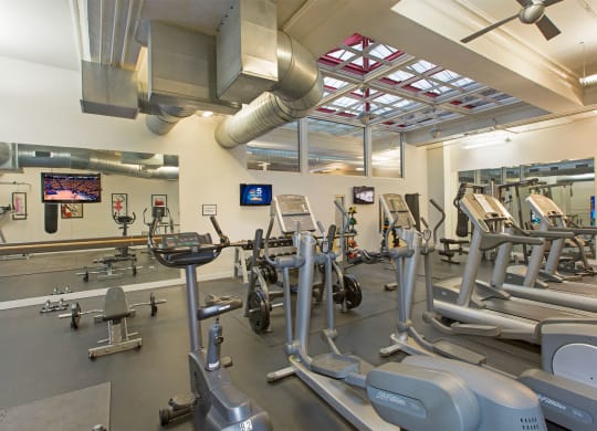 a gym with weights and cardio equipment and a tv