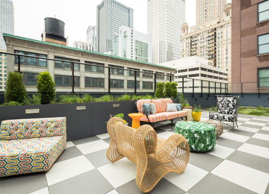 a rooftop lounge area with chairs and tables and skyscrapers