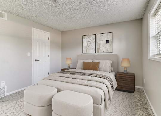 A bedroom with a large bed, two lamps, and two round ottomans.