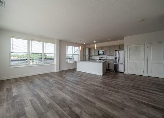 A spacious room with wooden flooring and a kitchen area in the background.