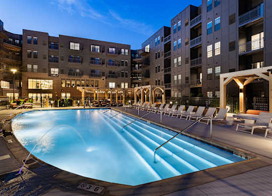 A large outdoor swimming pool surrounded by lounge chairs and buildings.