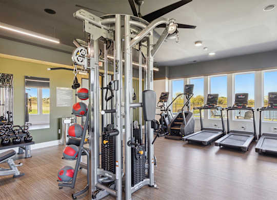 A gym with a variety of equipment including treadmills, weights, and a ceiling fan.