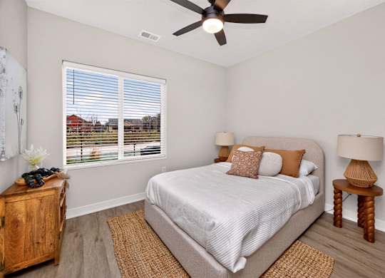 A bedroom with a bed, a ceiling fan, and a window with blinds.
