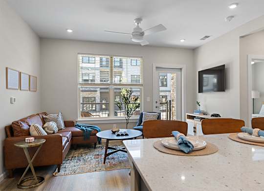 A living room with a brown leather couch and a white ceiling fan.
