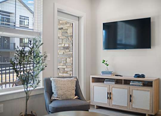 A living room with a grey couch, a wooden cabinet, and a flat screen TV mounted on the wall.
