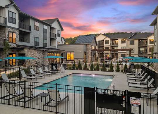 A swimming pool surrounded by lounge chairs and umbrellas in front of apartment buildings.