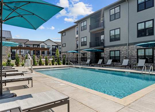 A swimming pool surrounded by lounge chairs and umbrellas in front of apartment buildings.
