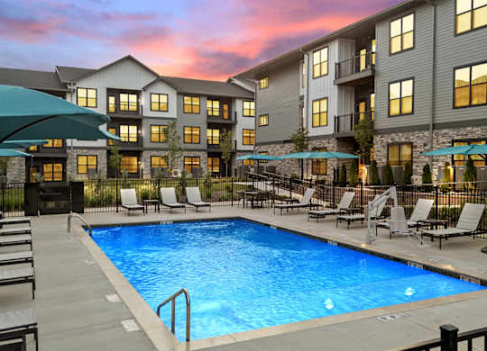 A swimming pool surrounded by lounge chairs and umbrellas in front of a building.