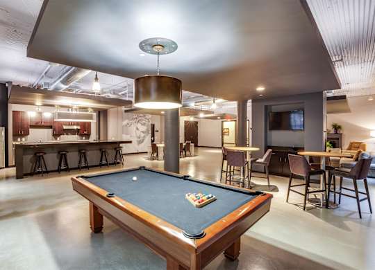 A pool table is in the middle of a room with a bar and a television.