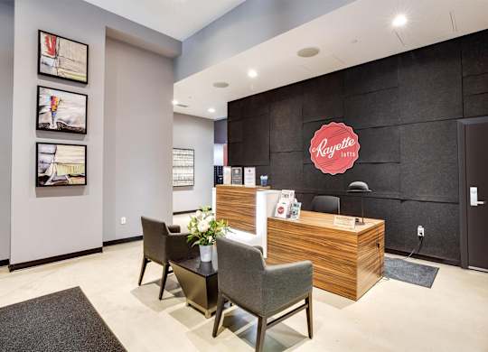 A reception area with a wooden desk and chairs, a potted plant, and pictures on the wall.