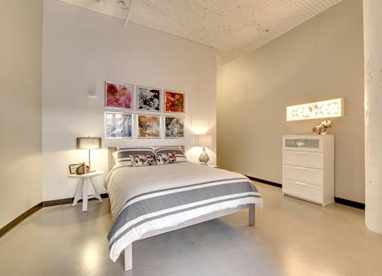 A bedroom with a bed, nightstand, and a white dresser.