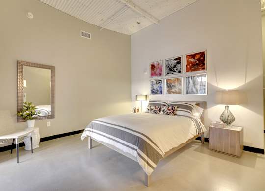 A bedroom with a large bed, a chair, a mirror, and a wall-mounted lamp.