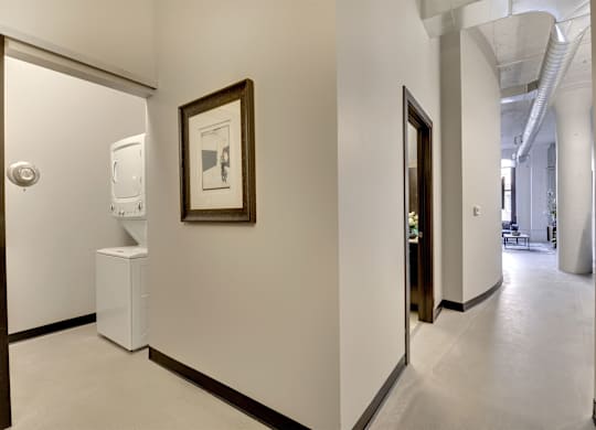 A hallway with a framed picture on the wall and a white trash can.