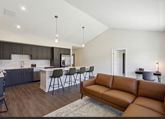 A modern living room with a brown leather couch and a kitchen area with a white counter.