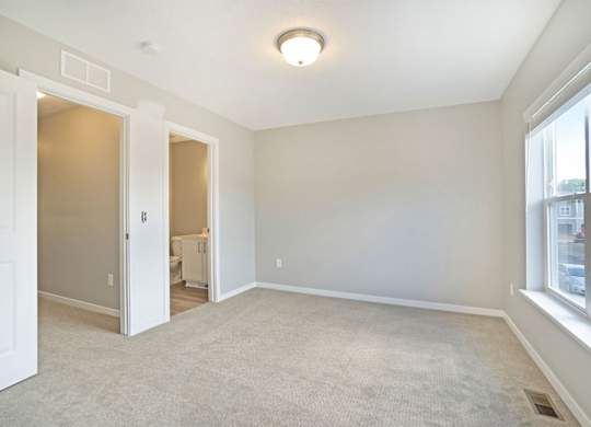 A spacious room with a carpeted floor and a window on the right side.