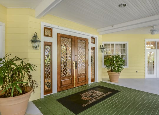 a front door with a green rug and two potted plantsat Arbor Oaks at Greenacres, Florida