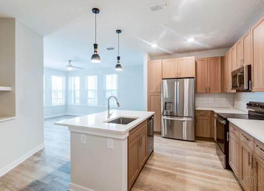 A kitchen with wooden cabinets and a white island at Tapestry Nona Apartments in Orlando, FL