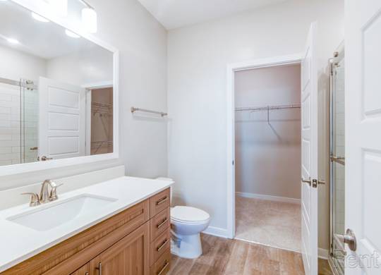 Ensuite bathroom with framed mirror, quartz countertops, and wood flooring at Tapestry Nona Apartments in Orlando, FL.