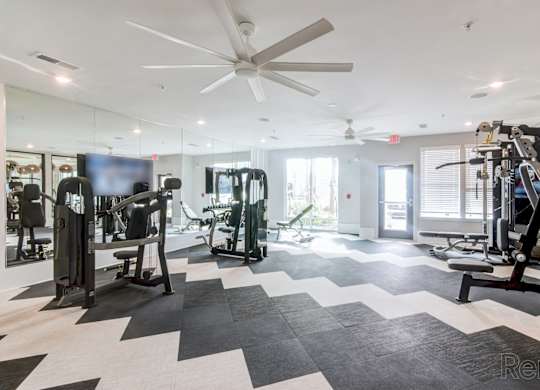 A spacious gym with a variety of equipment and a ceiling fan at Tapestry Nona Apartments in Orlando, FL