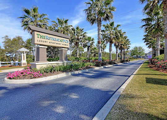 The entrance to The Retreat at Luxury Apartments is surrounded by palm trees and landscaping.