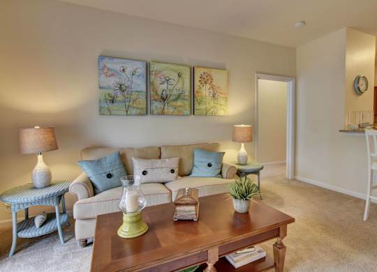 A living room with a white couch, a blue chair, a wooden coffee table, and a painting on the wall.