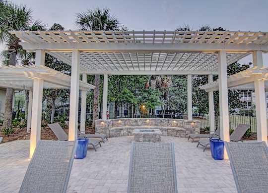 A white pergola with a stone fireplace underneath it.