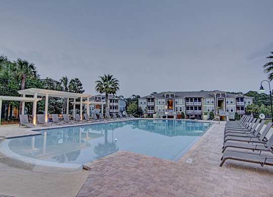 A large swimming pool surrounded by lounge chairs and a building in the background.