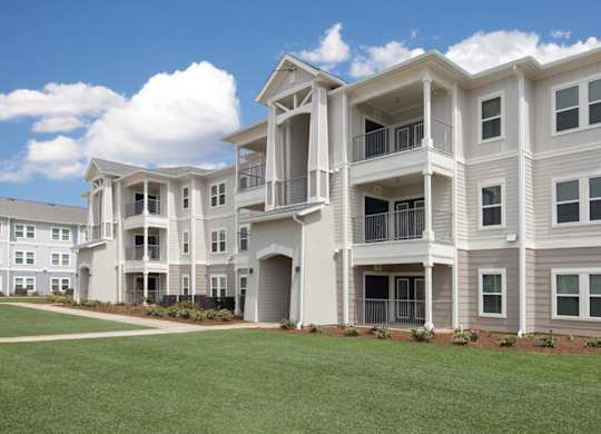 A large, modern apartment building with multiple balconies and a well-manicured lawn in front.