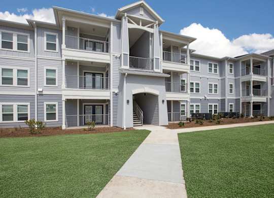 A large, modern apartment complex with a well-maintained lawn and clear skies.