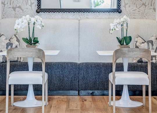 A dining room with a white table and chairs, a mirror, and a wallpapered wall.