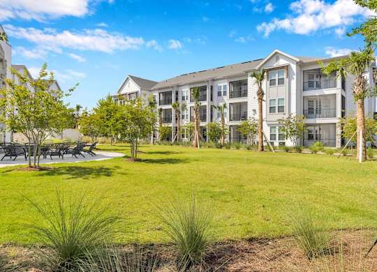 A large grassy area in front of a building with trees and benches.