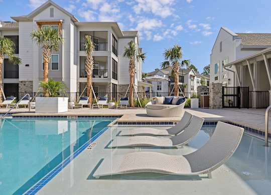 A pool with sun loungers and a building in the background.