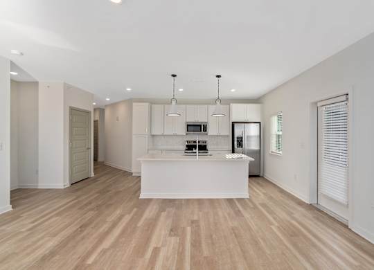 A spacious kitchen with wooden floors and white cabinetry.