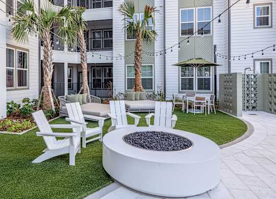 A white fire pit sits in the middle of a grassy area with white chairs around it.