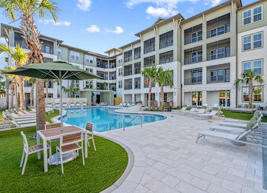 A pool area with a table and chairs and a building in the background.