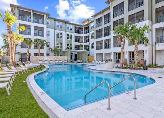 A swimming pool in front of a building with palm trees.