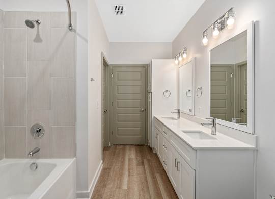 A bathroom with a white tub, sink, and a wooden floor.