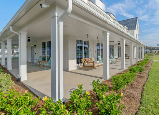 the front porch of a white house with columns and a porch swing at The Cottages at Foley Farms apartments in Foley, AL