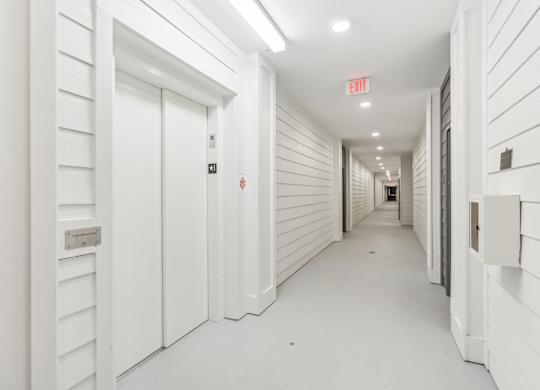 a long hallway with white doors and a exit sign