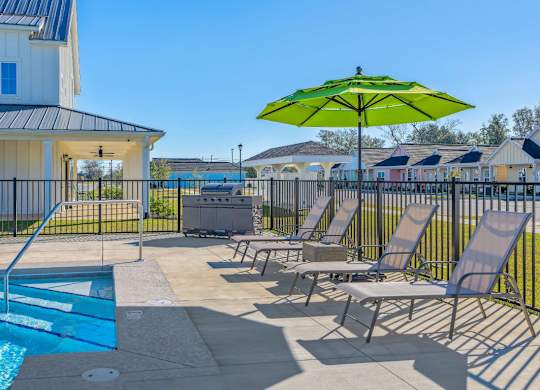 A pool area with a green umbrella and lounge chairs.
