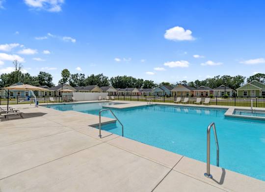 A large swimming pool surrounded by a concrete patio and lounge chairs.