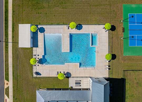 A pool surrounded by a concrete patio and a tennis court.